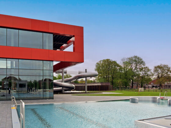 Moderne Schwimmhalle mit Rutsche und großzügigem Außenbereich in einer grünen Umgebung.