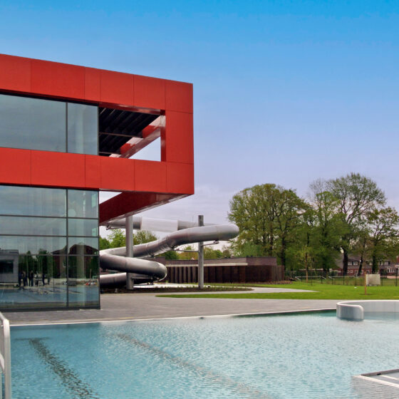 Moderne Schwimmhalle mit Rutsche und großzügigem Außenbereich in einer grünen Umgebung.