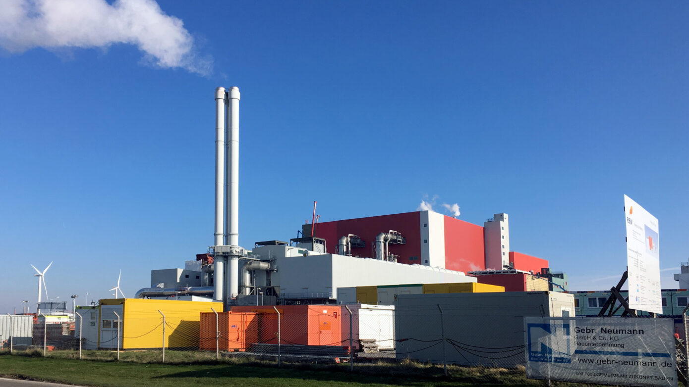 Ersatzbrennstoff-Heizkraftwerk Delfzijl mit Schornsteinen, Windkraftanlagen und bunten Containern unter blauem Himmel.