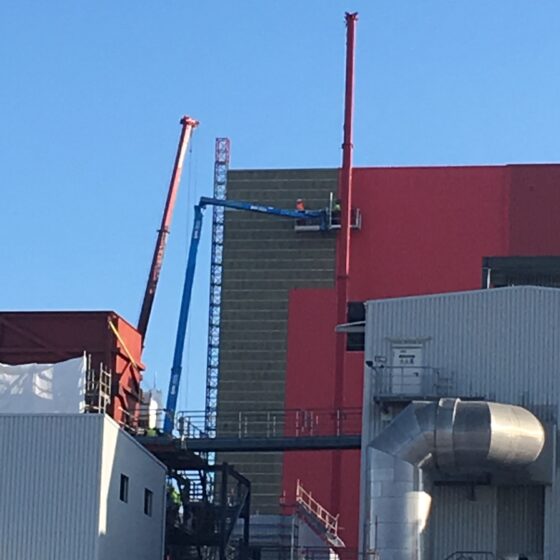 Arbeiter mit Kran an Industriegebäude für Wartungsarbeiten in blauem Himmel.