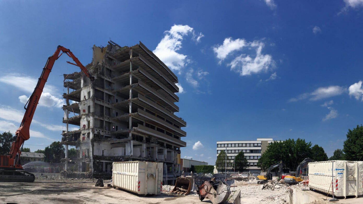 Abgerissenes Gebäude mit Bagger, Baustelle und blauen Himmel, Wolken im Hintergrund.