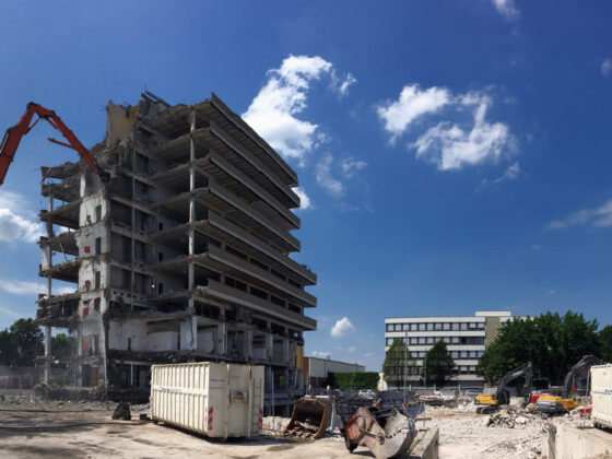 Abgerissenes Gebäude mit Bagger, Baustelle und blauen Himmel, Wolken im Hintergrund.