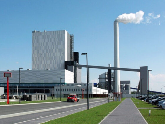Kraftwerk Wilhelmshaven mit rauchendem Schornstein und Parkplatz im Vordergrund.