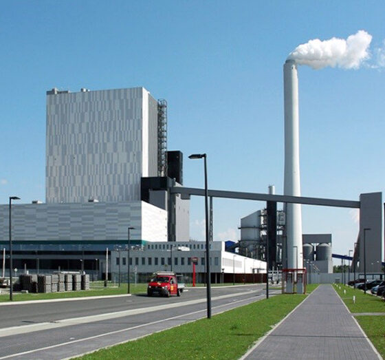 Kraftwerk Wilhelmshaven mit rauchendem Schornstein und Parkplatz im Vordergrund.