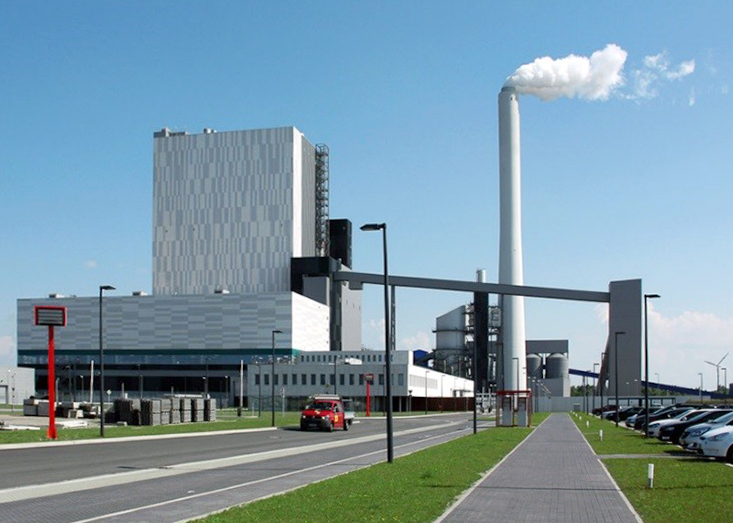 Kraftwerk Wilhelmshaven mit rauchendem Schornstein und Parkplatz im Vordergrund.