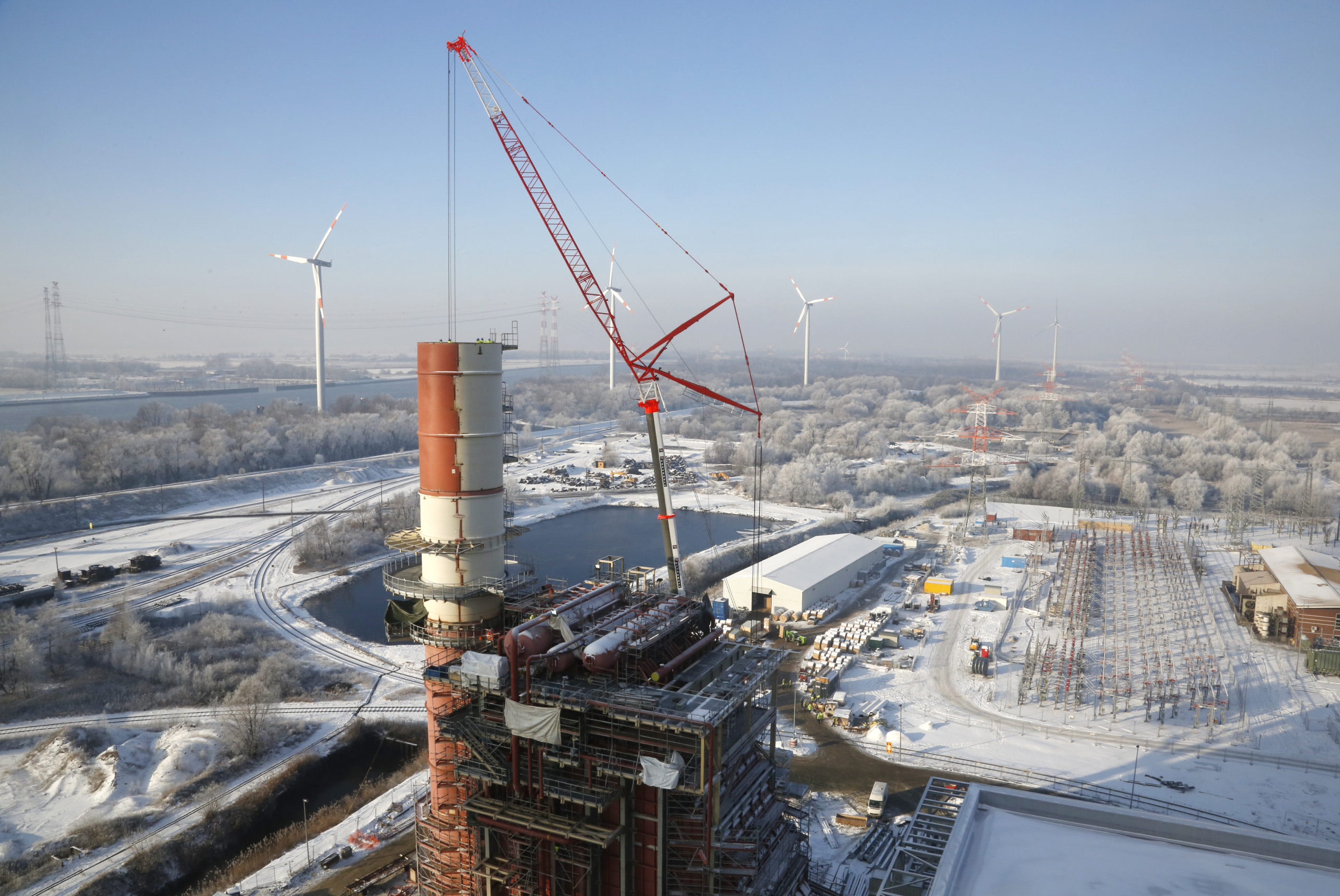 Bau des GuD-Kraftwerks im Winter mit Windkraftanlagen im Hintergrund.