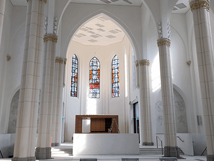 Helle Innenansicht einer Kirche mit bunten Fenstern und hohen Säulen.