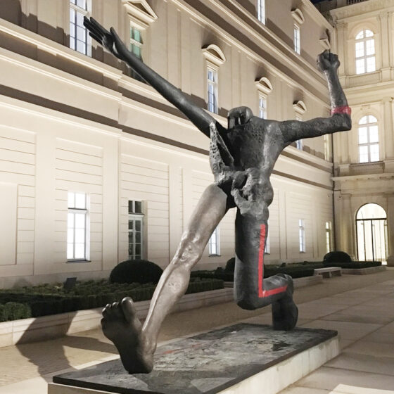 Moderne Skulptur eines dynamischen Tänzers vor einem eleganten Gebäude bei Nacht.