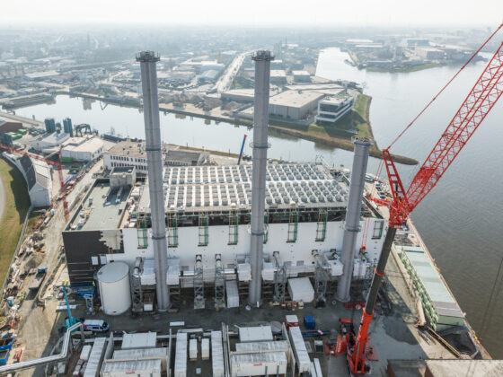 Blockheizkraftwerk Bremen Hastedt mit hohen Schornsteinen und Kran am Wasser.