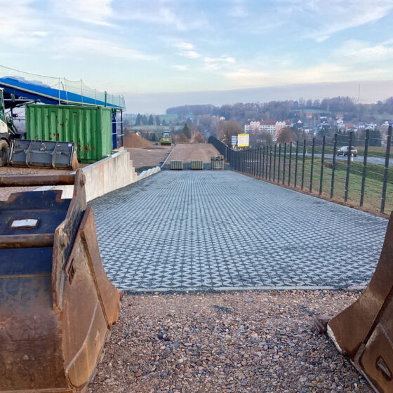Bauplatz mit Lkw, Baustellenfahrzeugen und befestigter Zufahrt in ländlicher Umgebung.