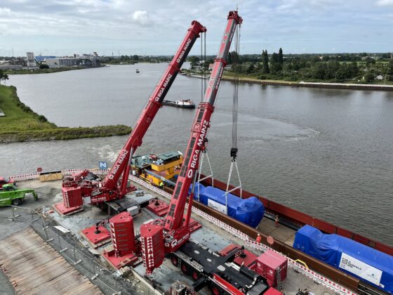 Rote Kräne heben Lasten an einem Flussufer, Bauarbeiten im Gange.
