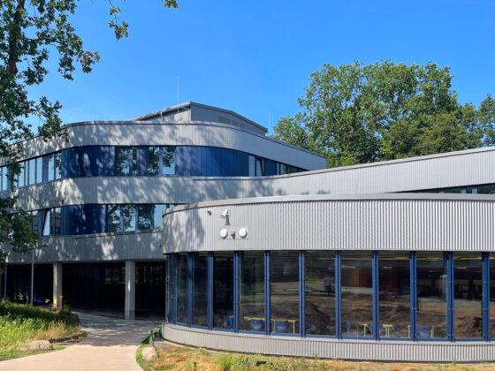 Moderne Architektur mit großen Fenstern und grünem Umfeld unter blauem Himmel.
