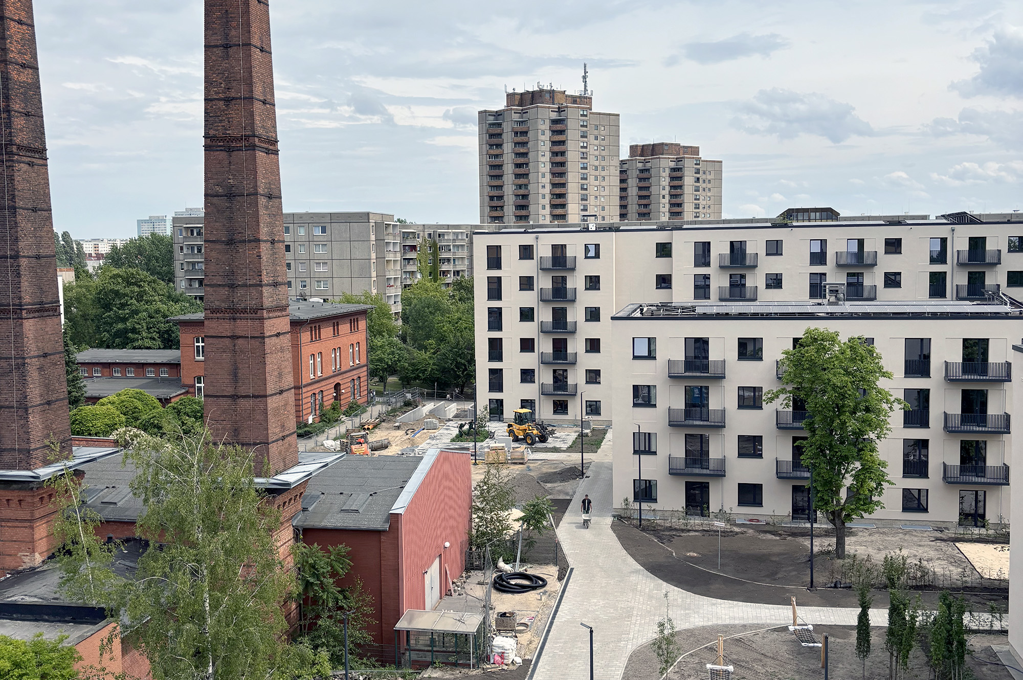 Städtische Bauarbeiten mit modernen Wohnanlagen und historischen Fabrikschornsteinen in der Umgebung.
