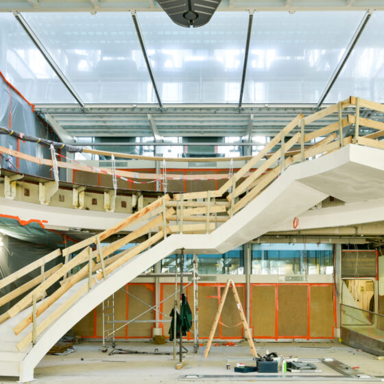Moderne Treppe im Bau mit Holzgeländer und Glasdach in einem Innenraum.