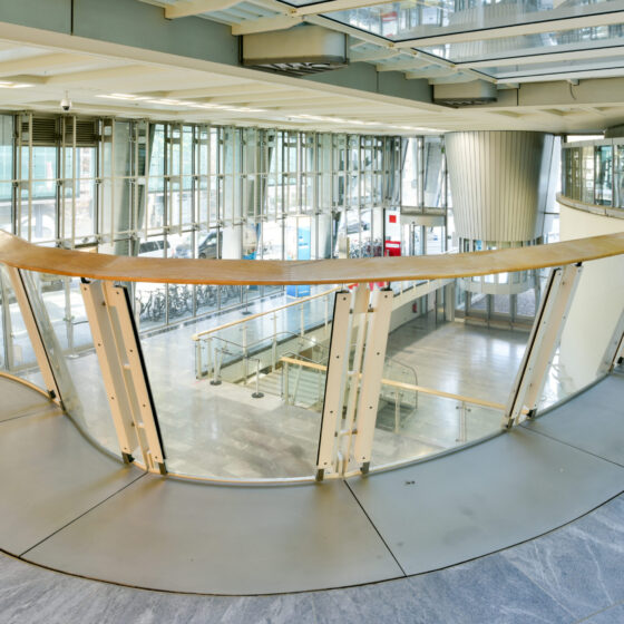 Moderne Architektur mit Glaswänden und geschwungener Holzbrüstung in einem Innenraum.