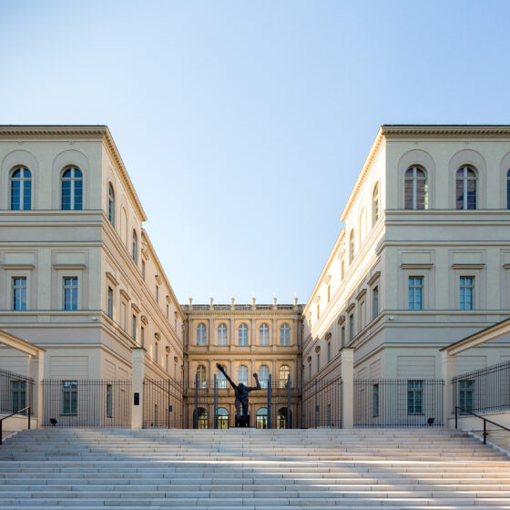 Museum Barberini mit Treppen und Skulptur, umgeben von klarem Himmel.
