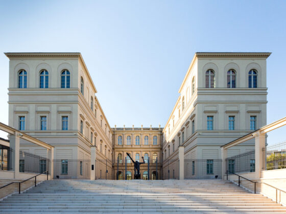 Museum Barberini mit Treppen und Skulptur, umgeben von klarem Himmel.