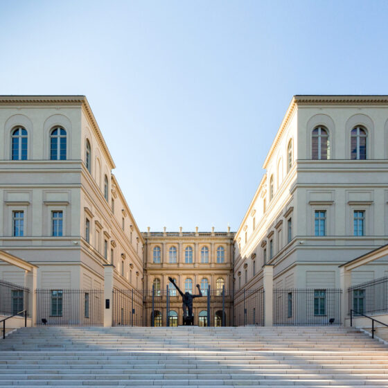 Museum Barberini mit Treppen und Skulptur, umgeben von klarem Himmel.