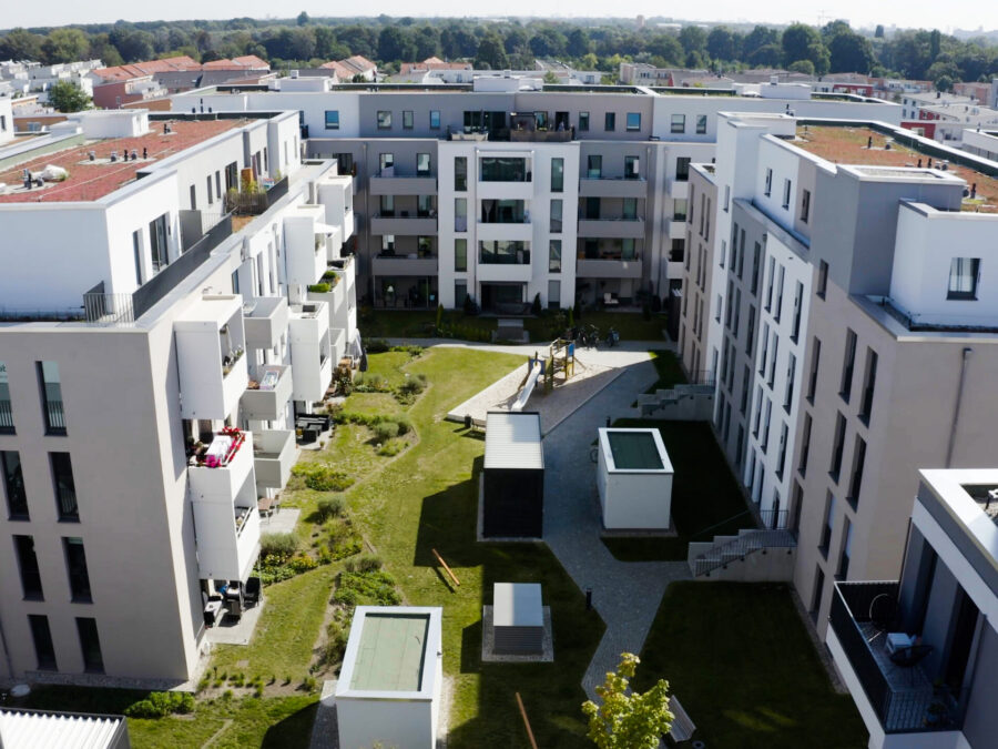 Moderne Wohnanlage mit Innenhof, Grünflächen und Spielplatz in urbaner Umgebung.