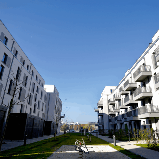 Moderne Wohnanlage mit Balkonen, grüner Fläche und klarem blauen Himmel.