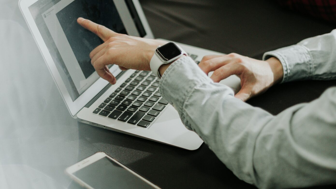 Mann zeigt auf Laptop-Bildschirm während einer Besprechung am Tisch.