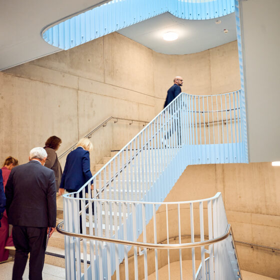 Moderne Treppe mit geschwungenem Geländer und Personen, die nach oben gehen.