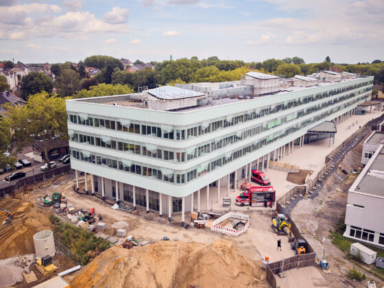 Moderne Bauarbeiten an einem neuen Gebäudekomplex mit Baustellenfahrzeugen und Grünflächen.