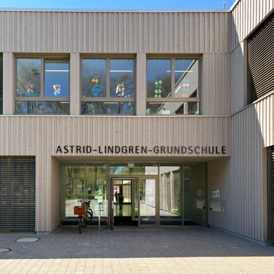 Eingang der Astrid-Lindgren-Grundschule mit moderner Holzfassade und bunten Fenstern.