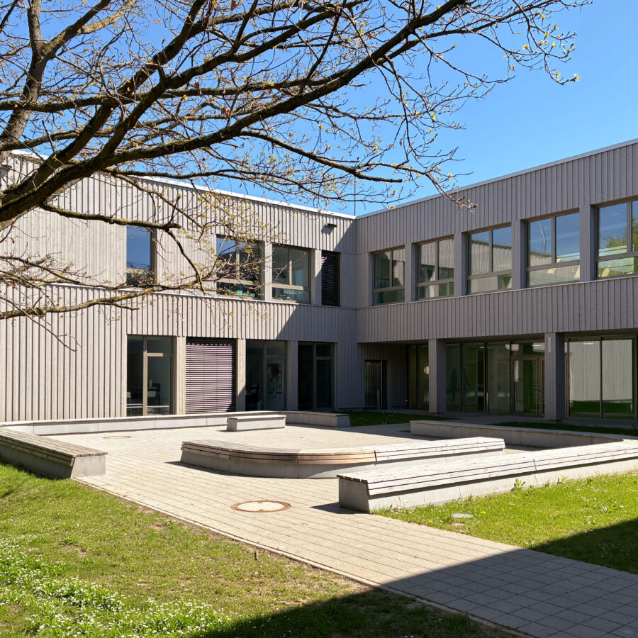 Gebäude der Astrid-Lindgren-Grundschule mit Innenhof und Grünflächen unter blauem Himmel.