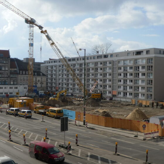 Bauarbeiten in der Stadt mit Kränen, Baustellenfahrzeugen und neuen Wohngebäuden.
