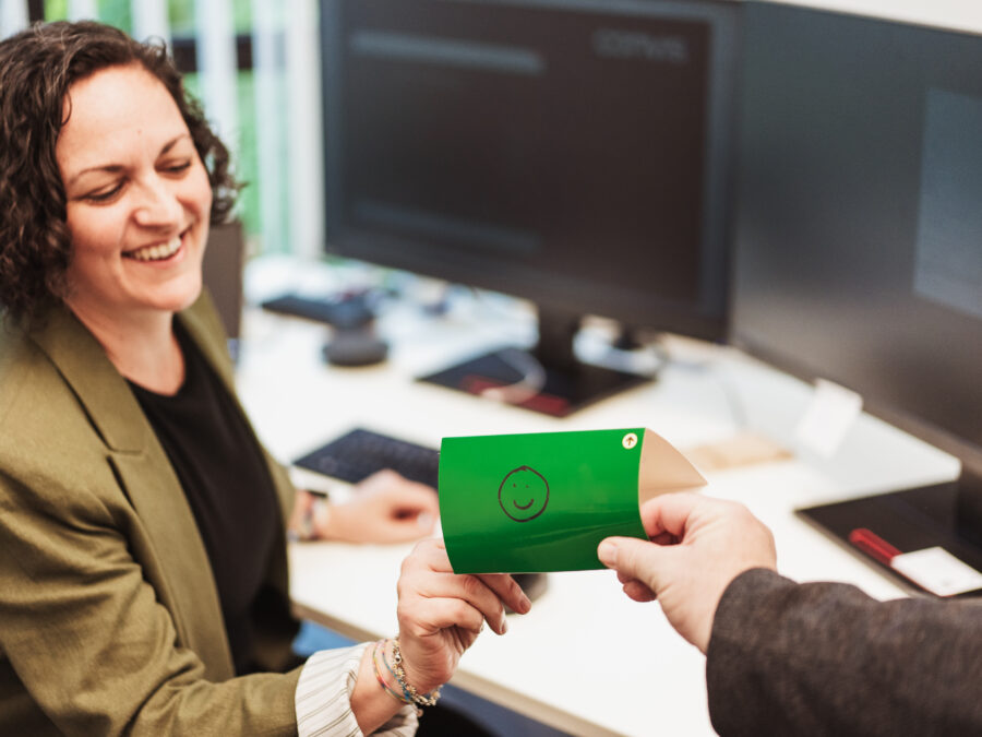 Frau lächelt beim Empfang eines grünen Umschlags in einem modernen Büro.