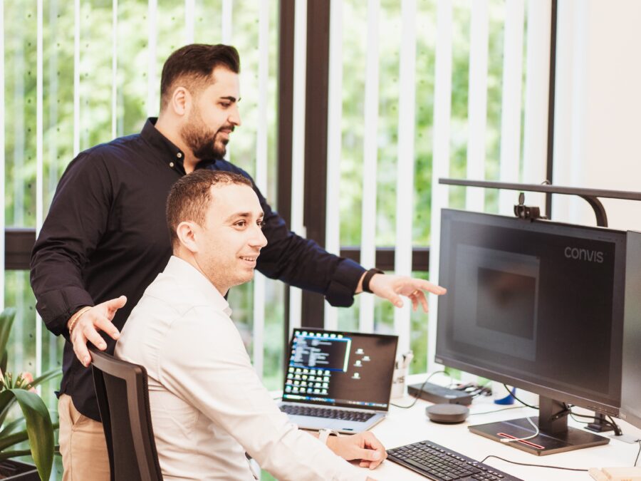 Zwei Männer im Büro, einer erklärt etwas am Computer, moderne Arbeitsumgebung.