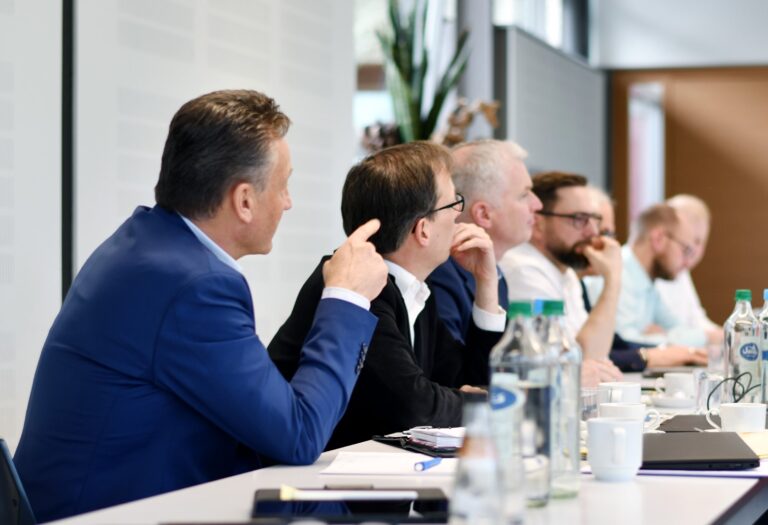 Geschäftsmeeting mit mehreren Teilnehmern an einem Tisch in modernem Konferenzraum.