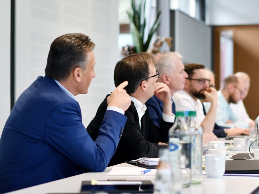 Geschäftsmeeting mit mehreren Teilnehmern an einem Tisch in modernem Konferenzraum.