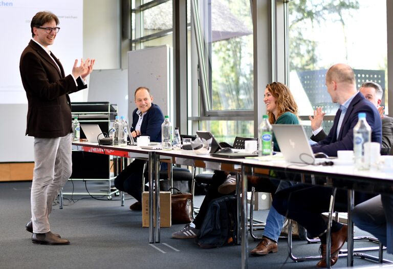 Teammeeting mit Präsentation: Teilnehmer diskutieren aktiv in modernem Konferenzraum.