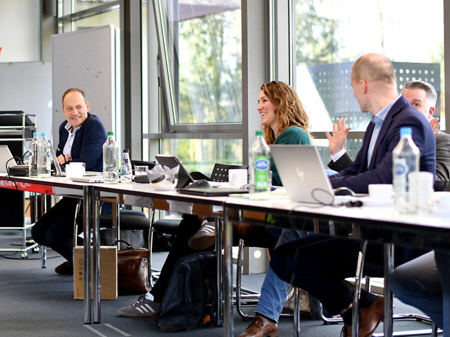 Teammeeting mit Präsentation: Teilnehmer diskutieren aktiv in modernem Konferenzraum.