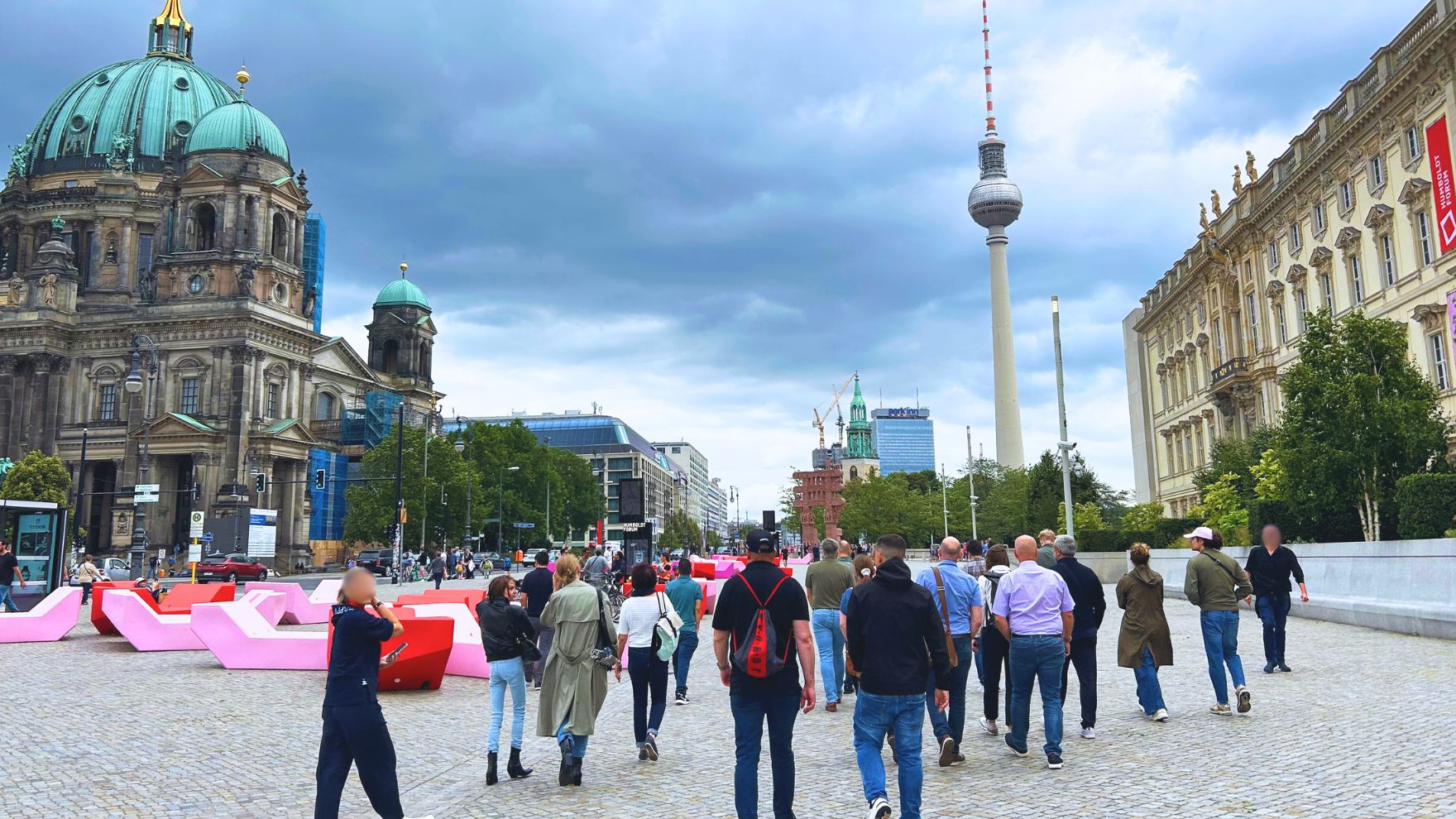 Menschen schlendern durch Berlin, mit dem Berliner Dom und Fernsehturm im Hintergrund.