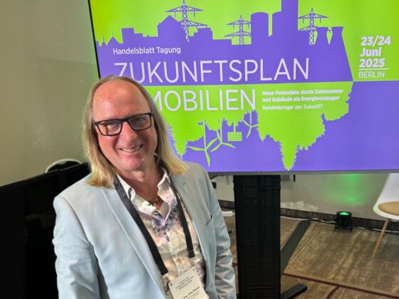 Mann steht vor Bildschirm mit dem Titel "Zukunftsplan Mobilien" auf einer Tagung in Berlin.