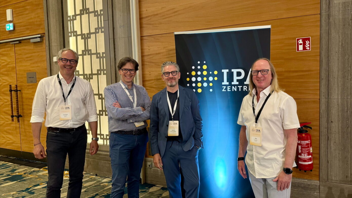 Vier Fachleute stehen vor einem Banner des IPZentrums auf einer Veranstaltung.
