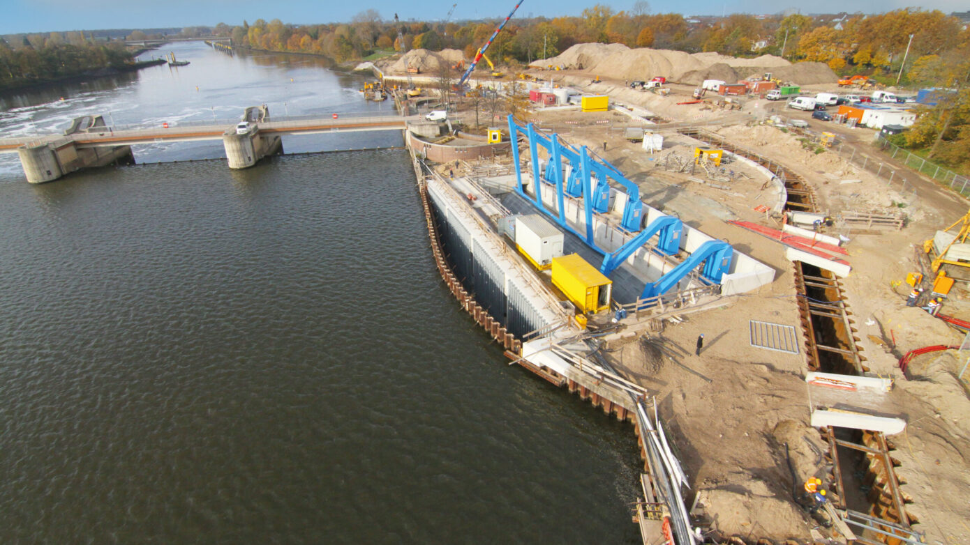 Bauarbeiten an einer Schleuse mit blauen Maschinen und Wasserweg im Hintergrund.