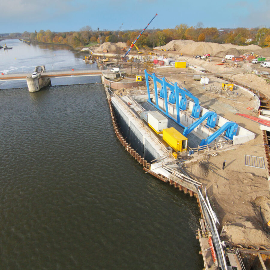 Bauarbeiten an einer Schleuse mit blauen Maschinen und Wasserweg im Hintergrund.
