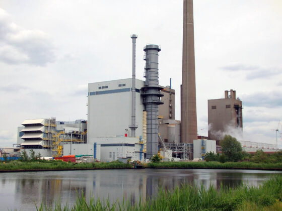 GUD-Kraftwerk mit Kühlturm und Produktionsgebäude am Wasser, umgeben von grüner Vegetation.