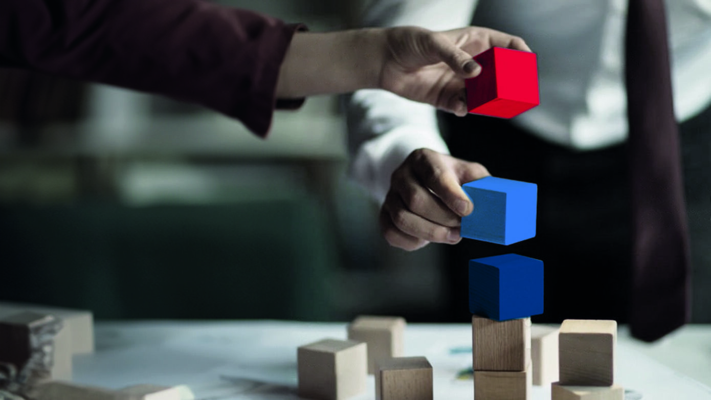 Mann stapelt bunte Blöcke auf einem Tisch mit kreativen Materialien.