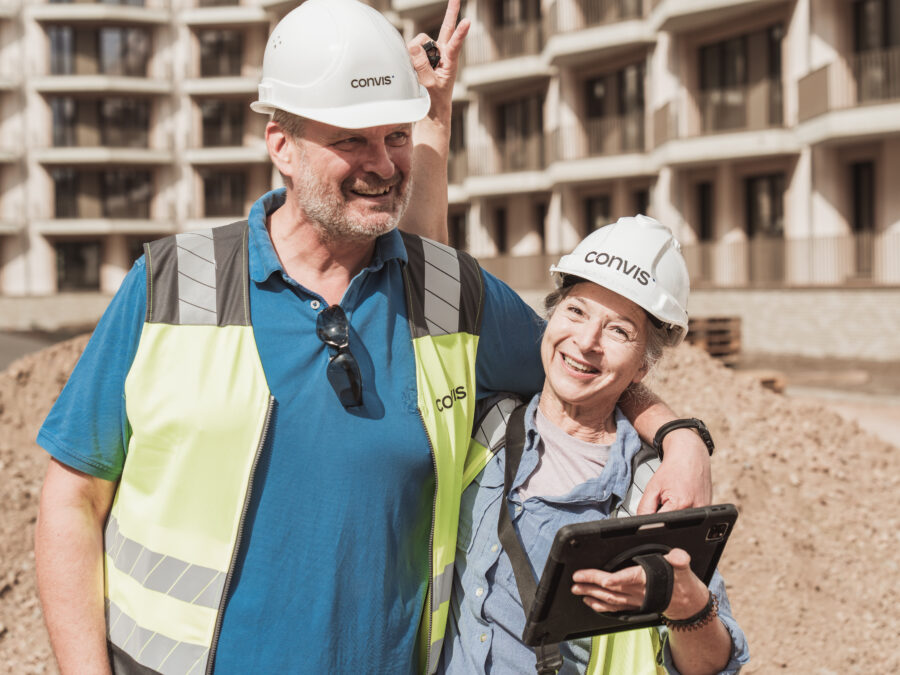 Bauarbeiter mit Helmen und Sicherheitswesten lächeln auf einer Baustelle.