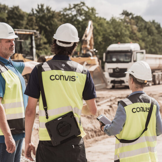 Bauleiter besprechen Projektfortschritt auf Baustelle mit Baumaschinen im Hintergrund.