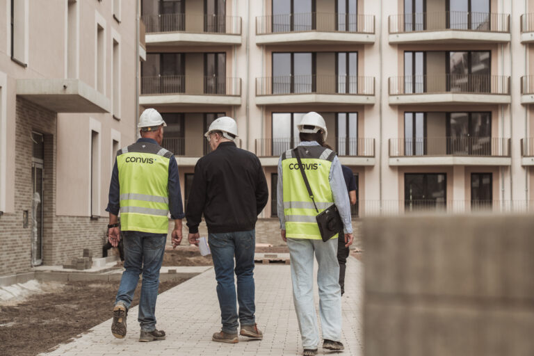 Bauarbeiter in Sicherheitswesten und Helmen auf einer Baustelle mit modernen Wohngebäuden.