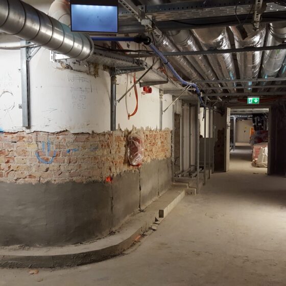 Bauarbeiten in einem Flur mit freiliegenden Wänden und Kabeln.