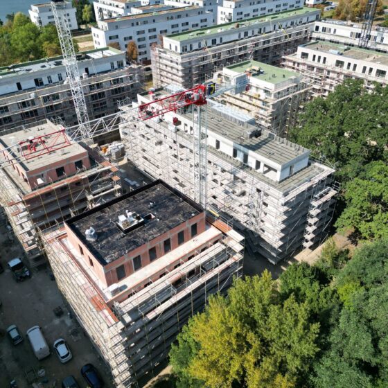 Bauarbeiten an modernen Wohngebäuden mit Gerüsten und Kränen in städtischer Umgebung.