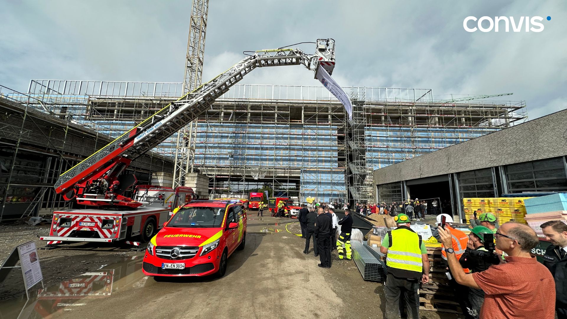 Feuerwehr im Einsatz bei einem Bauprojekt, Rettungsübung mit Drehleiter und Zuschauern.