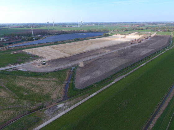 Bauarbeiten auf einem großen Grundstück mit Windkraftanlagen im Hintergrund.